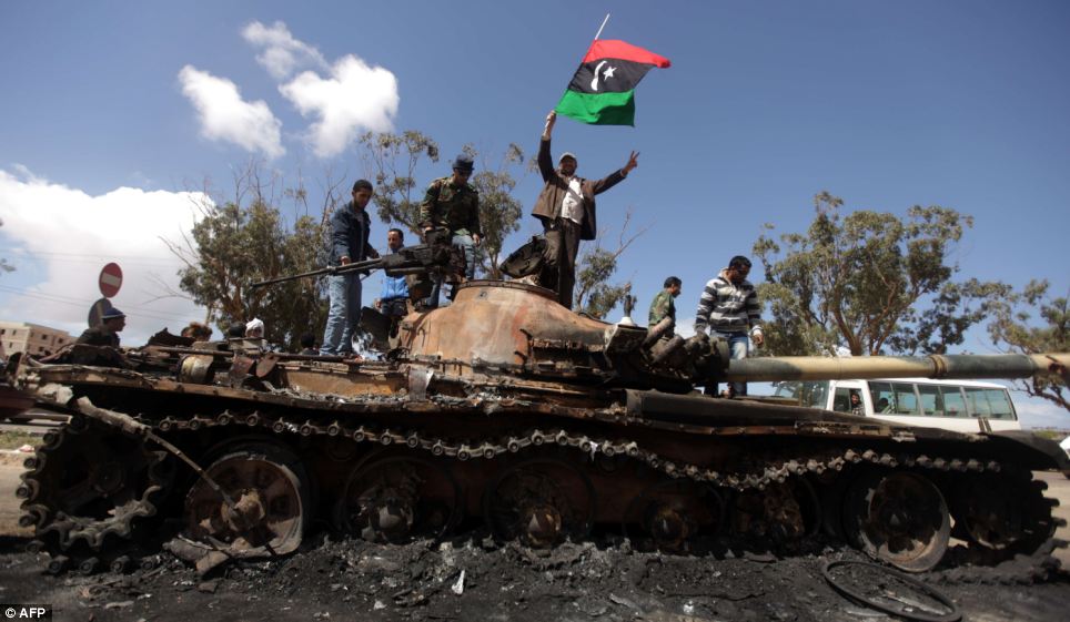 Libyan rebels wave their flag on top of the charred remains of a wrecked tank belonging to Moammar Gadhafi's forces at the western entrance to Benghazi, Libya. (photo credit: AFP)