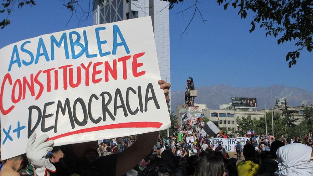 A protester in Santiago holds a sign calling for a 'constitutional assembly for more democracy' [photo credit: Sandra Cuffe/Al Jazeera]